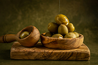 Small bowl filled with green olives on a wooden cutting board.