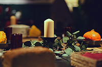 Cozy table setting with a candle in the center, surrounded
                        by scattered green leaves and simple place settings.